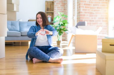 Genç ve cüsseli bir kadın karton kutuların etrafında yerde oturuyor. Yeni bir eve taşınıyor. Sevgiyle gülümsüyor. Romantik konsept.