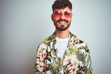 Tatilde dövmeli, güneş gözlüklü, izole edilmiş beyaz arka planda mutlu ve havalı bir gülümsemesi olan bir adam. Şanslı kişi..