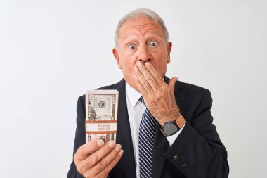Kıdemli gri saçlı işadamı, dolar tutan takım elbiseli, izole edilmiş beyaz arka planda, ağzı kapalı, utançtan ağzı açık, korkunun ifadesi, sessizlikten korkan, gizli bir konsept.