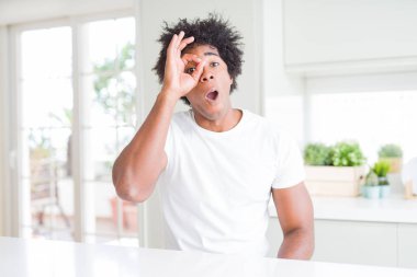 Beyaz günlük tişörtler giyen Afro-Amerikan genç bir adam evinde oturmuş şaşırmış yüz ifadesiyle şaşırmış, parmaklarından bakan bir jest yapıyor. İnançsız ifade.