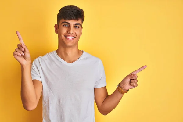 白いTシャツを着た若いインド人男性が 黄色の背景の上に立って 自信を持ってさまざまな方向への指で指して笑っている 広告のコピースペース — ストック写真