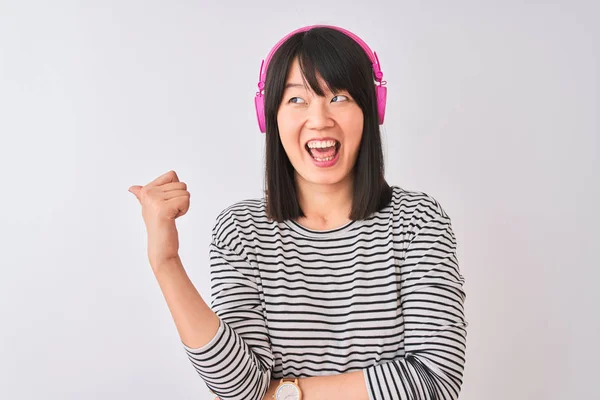 中国妇女在孤独的白色背景下 用粉色耳机听着音乐 面带微笑 面带微笑 并竖起大拇指指向一边 — 图库照片