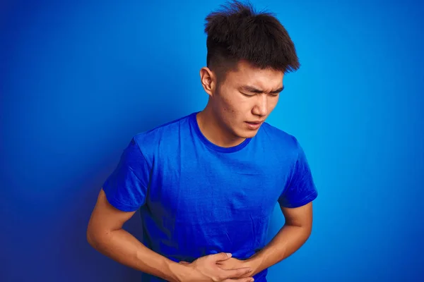 若いアジア系中国人男性のTシャツを着て 胃の上に手で隔離された青の背景の上に立って消化不良 痛みを伴う病気の気分が悪い アチェの概念 — ストック写真