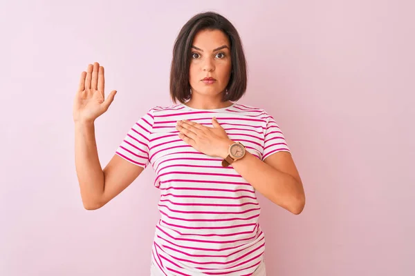 年轻美丽的女人穿着条纹T恤 站在孤立的粉色背景上 双手放在胸前 张开手掌 发誓效忠 — 图库照片