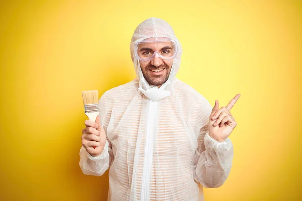 Joven Hombre Vistiendo Equipo Pintor Sosteniendo Pincel Pintura Sobre Fondo — Foto de Stock