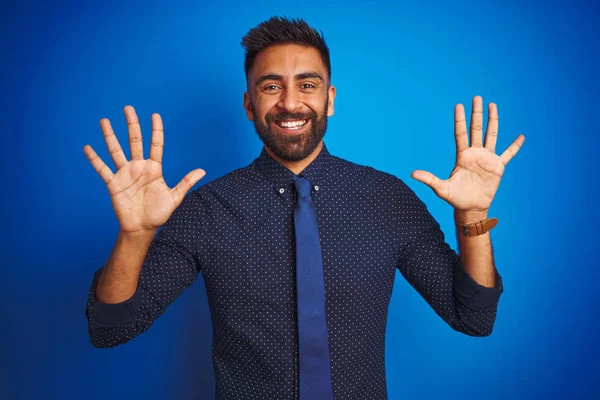 エレガントなシャツを着て独立した青の背景の上に立ってネクタイを身に着けている若いインドのビジネスマンは自信と幸せ笑顔ながら指の数10で示すと指摘 — ストック写真