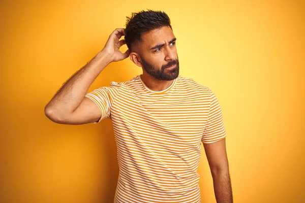 孤立した黄色の背景の上に立ってTシャツを着て若いインド人男性は混乱し 質問について疑問に思います 疑いもなく 頭の上で手で考えて 包括的概念 — ストック写真