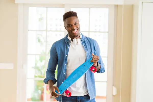 Knappe Afrikaanse jonge hipster man Holding skateboard glimlachend, t — Stockfoto
