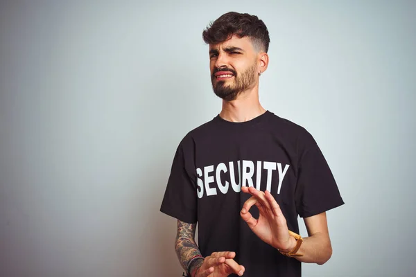 Young safeguard man with tattoo wering security uniform over isolated white background disgusted expression, displeased and fearful doing disgust face because aversion reaction. With hands raised. Annoying concept.
