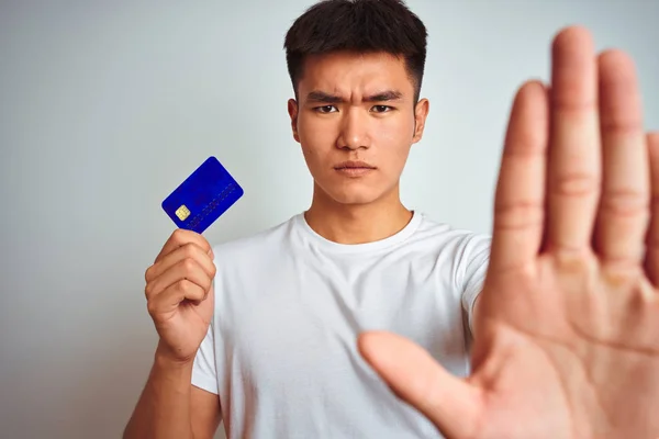 年轻的亚裔男子持信用卡站在孤立的白色背景上 张开双手 做着手势 严肃而自信地表达着防守的姿态 — 图库照片