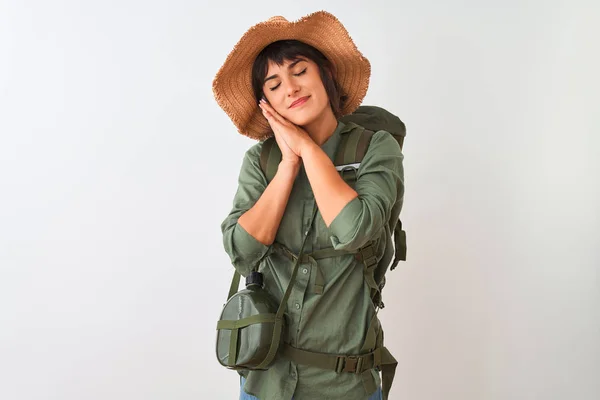 Hiker woman wearing backpack hat and water canteen over isolated white background sleeping tired dreaming and posing with hands together while smiling with closed eyes.