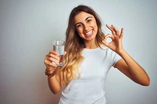 若いです美しい女性飲料水のガラスの上に白い隔離された背景を行います指でOkサイン 優れたシンボル — ストック写真