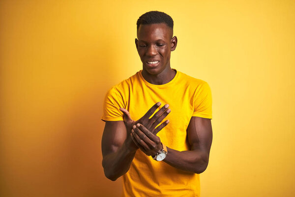 Young african american man wearing casual t-shirt standing over isolated yellow background Suffering pain on hands and fingers, arthritis inflammation