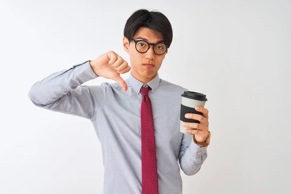 Chinese businessman wearing tie and glasses drinking coffee over isolated white background with angry face, negative sign showing dislike with thumbs down, rejection concept