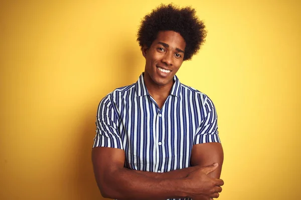 American man with afro hair wearing striped shirt standing over isolated yellow background happy face smiling with crossed arms looking at the camera. Positive person.