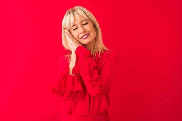 Middle age woman wearing elegant shirt standing over isolated red background sleeping tired dreaming and posing with hands together while smiling with closed eyes.