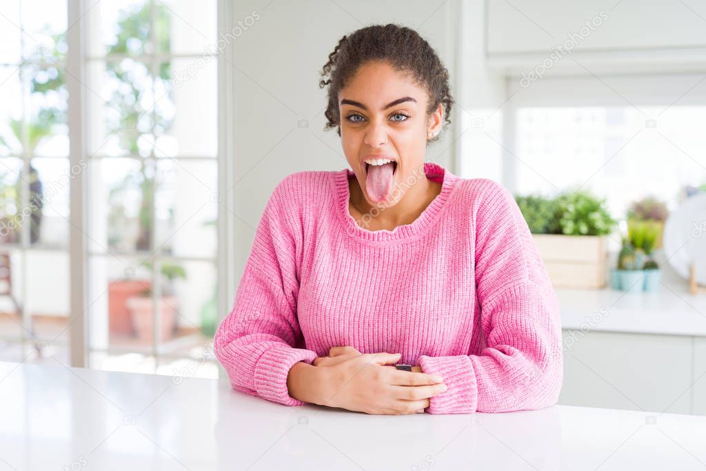 Beautiful african american woman with afro hair wearing casual pink sweater sticking tongue out happy with funny expression. Emotion concept.