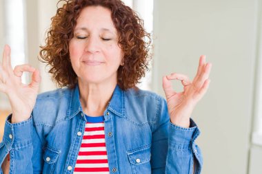 Güzel bir son sınıf öğrencisi kadın rahatlar ve gözleri kapalı gülümser parmaklarıyla meditasyon jesti yapar. Yoga konsepti.