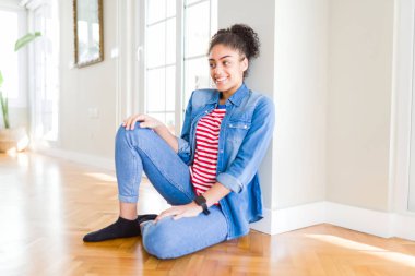 Afro saç ile güzel genç Afrikalı Amerikalı kadın katta oturan yüzünde gülümseme ile yan bakıyor, doğal ifade. Güven gülüyor.