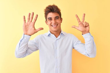 Genç yakışıklı iş adamı zarif bir gömlek giyerek izole edilmiş sarı arka plan üzerinde 8 numaralı parmaklarıyla işaret ederken kendinden emin ve mutlu bir şekilde gülümsüyor..