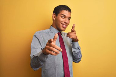 İzole edilmiş sarı arka plan üzerinde gömlek ve kravat takan genç yakışıklı Arap işadamı mutlu ve komik yüzlü parmaklarını kameraya doğrultuyor. İyi enerji ve titreşimler.