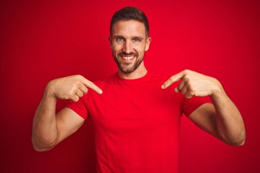Kırmızı izole edilmiş arka planda rahat bir tişört giyen genç yakışıklı yüzünde bir gülümsemeyle, gururlu ve mutlu bir şekilde kendini gösteren bir adam..