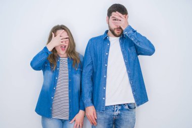 Genç ve güzel bir çift, beyaz izole edilmiş arka planda yan yana durur. Şoka girer, yüzlerini ve gözlerini kapar, utanmış bir ifadeyle parmaklarından bakar..