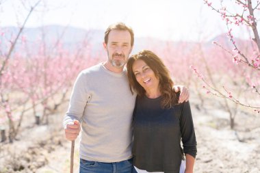 Baharın güneşli bir gününde pembe yaprakları ile şeftali ağaçlarının romantik bahçesinde aşık gülümseyen güzel orta yaş yaşlı çift