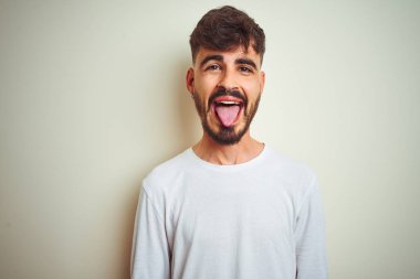 İzole edilmiş beyaz arka plan üzerinde duran dövmeli genç adam komik bir ifadeyle dilini dışarı çıkartıyor. Duygu kavramı.