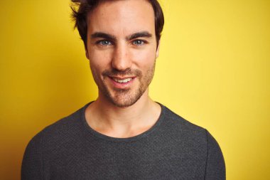 İzole edilmiş sarı arka planda dikilen sıradan süveter giyen genç yakışıklı bir adam mutlu bir yüzü olan ve kendine güvenen bir gülümsemeyle dişlerini gösteren.