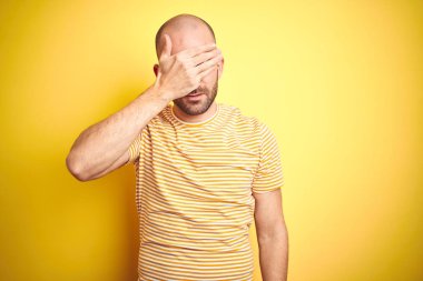 Sakallı, sarı renkli tişörtlü genç ve kel bir adam. Gözlerine el sürmüş, ciddi ve üzgün görünüyor. Görme, saklama ve reddetme konsepti