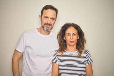 Yüzlerinde ciddi bir ifade olan soyutlanmış beyaz arka planda birlikte duran orta yaşlı güzel bir çift. Basit ve doğal bir şekilde kameraya bakıyorsun..