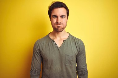 Sıradan tişörtler giyen genç yakışıklı adam izole edilmiş sarı arka planda durmuş komik yüzlü yanakları şişiriyor. Havayla şişmiş ağız, çılgın bir ifade..