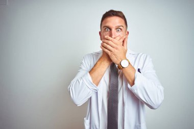 İzole arka planda beyaz kürk giyen yakışıklı doktor yanlışlıkla ağızlarını kapatarak şok etti. Gizli konsept.