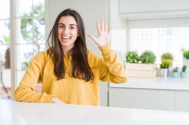 Sarı süveter giyen güzel genç bir kadın beş numarayı gösterip işaret ederken kendinden emin ve mutlu bir şekilde gülümsüyor..