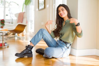 Genç güzel kadın evde katta oturan yüzünde gülümseme ile emin görünümlü, parmakları gururlu ve mutlu kendini işaret.