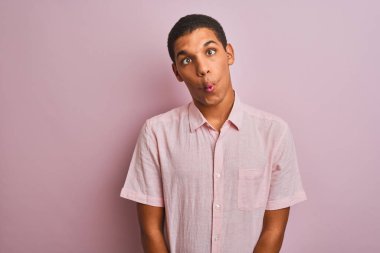 İzole edilmiş pembe arka plan üzerinde duran sıradan gömlekli genç yakışıklı Arap adam dudaklı balık suratı yapıyor, çılgınca ve komik bir jest. Komik ifade.