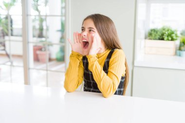 Güzel genç kız çocuk masada bağırarak oturan ve ağız da el ile yan yüksek sesle bağırıyor. İletişim kavramı.