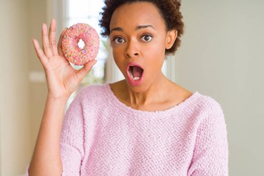 Pembe şekerli çörek yiyen genç afrikalı kadın sürpriz bir yüzle şokta korkmuş, korkuyla korkmuş ve heyecanlı ifade