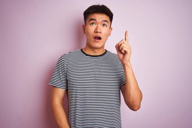 Soyutlanmış pembe arka planda duran çizgili tişört giyen Asyalı genç adam başarılı bir fikir olduğunu işaret ediyor. Heyecanlı ve mutlu. Bir numara..