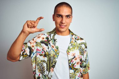 Tatilde, beyaz arka planda Hawaii gömleği giymiş, gülümseyen ve el hareketleriyle küçük boy işaretler yapan, parmaklarıyla kameraya bakan genç ve yakışıklı bir adam. Ölçü kavramı.