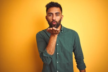 Zarif bir gömlek giyen genç Hintli işadamı izole edilmiş beyaz arka planda dikilip kameraya bakarak havada bir öpücük savuruyor ve sevimli ve seksi oluyor. Aşk ifadesi.