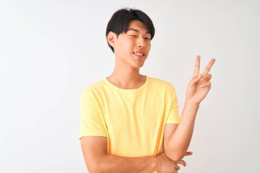 Sarı günlük tişört giyen Çinli bir adam izole edilmiş beyaz arka planda dikiliyor ve kameraya gülümsüyor zafer işareti yapıyor. İki numara..