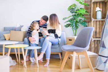 Güzel aile, anne-babalar kanepede kahve içme oturmuş karton kutular etrafında yeni evde oynayan çocuğuna bakıyor