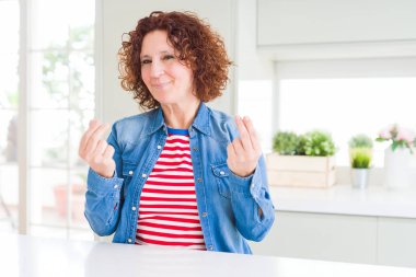 Orta yaşlı, kıvırcık saçlı, kot ceket giyen, elleriyle para hareketi yapan, maaşını isteyen, milyonerlik işi yapan bir kadın.