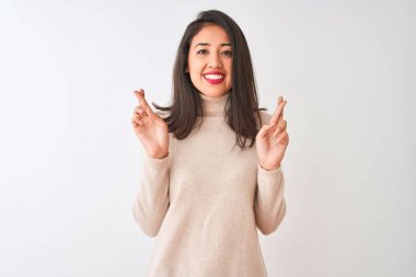 Balıkçı yaka kazak giyen güzel Çinli kadın izole edilmiş beyaz arka plan üzerinde duruyor umut ve gözler kapalı gülümseyerek el işareti yapıyor. Şans ve batıl inanç..