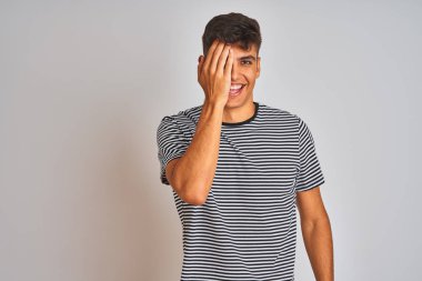 Genç Hintli adam donanma çizgili tişört giyiyor. İzole edilmiş beyaz arka planda duruyor. Bir gözünü eliyle kapatıyor..