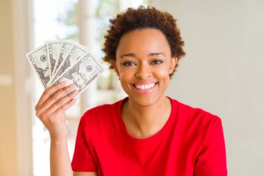 Genç Afrikalı Amerikalı kadın elinde 20 dolarlık banknotlar tutuyor. Mutlu bir yüzü var ve gülümsüyor. Kendine güvenen bir gülümsemeyle dişlerini gösteriyor.
