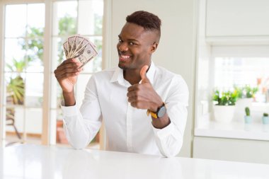 Afro-amerikan adam elli dolar banka notları tutan büyük bir gülümseme ok işareti yapıyor mutlu, parmakları ile başparmak, mükemmel işareti