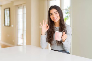 Bir fincan kahve içen genç bir kadın parmaklarıyla imza atıyor, mükemmel bir sembol.